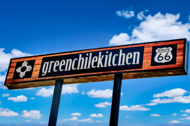 A green chile kitchen sign against a blue sky backdrop.