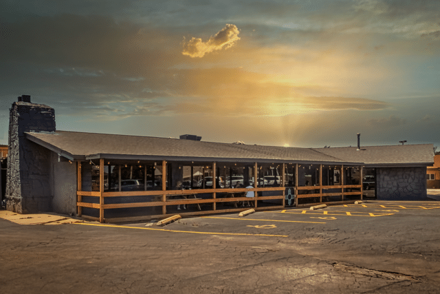 The Green Chile Kitchen with a parking lot and a sun setting behind it.