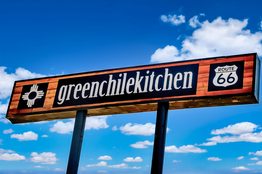 A green chile kitchen sign against a blue sky backdrop.