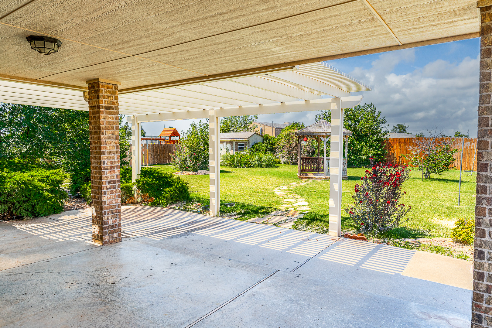 A covered patio in a backyard with a brick wall.