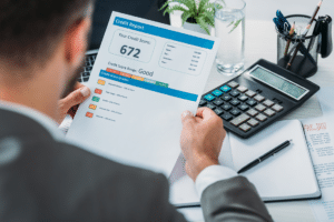 A man in a suit is analyzing the impact of credit score on mortgage rates alongside a calculator.