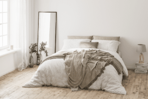 Small space staging: A minimalistic bedroom featuring a white bed and wooden floor design.