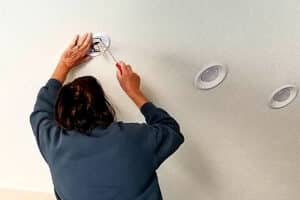 A woman demonstrating home maintenance tips by replacing a smoke detector.