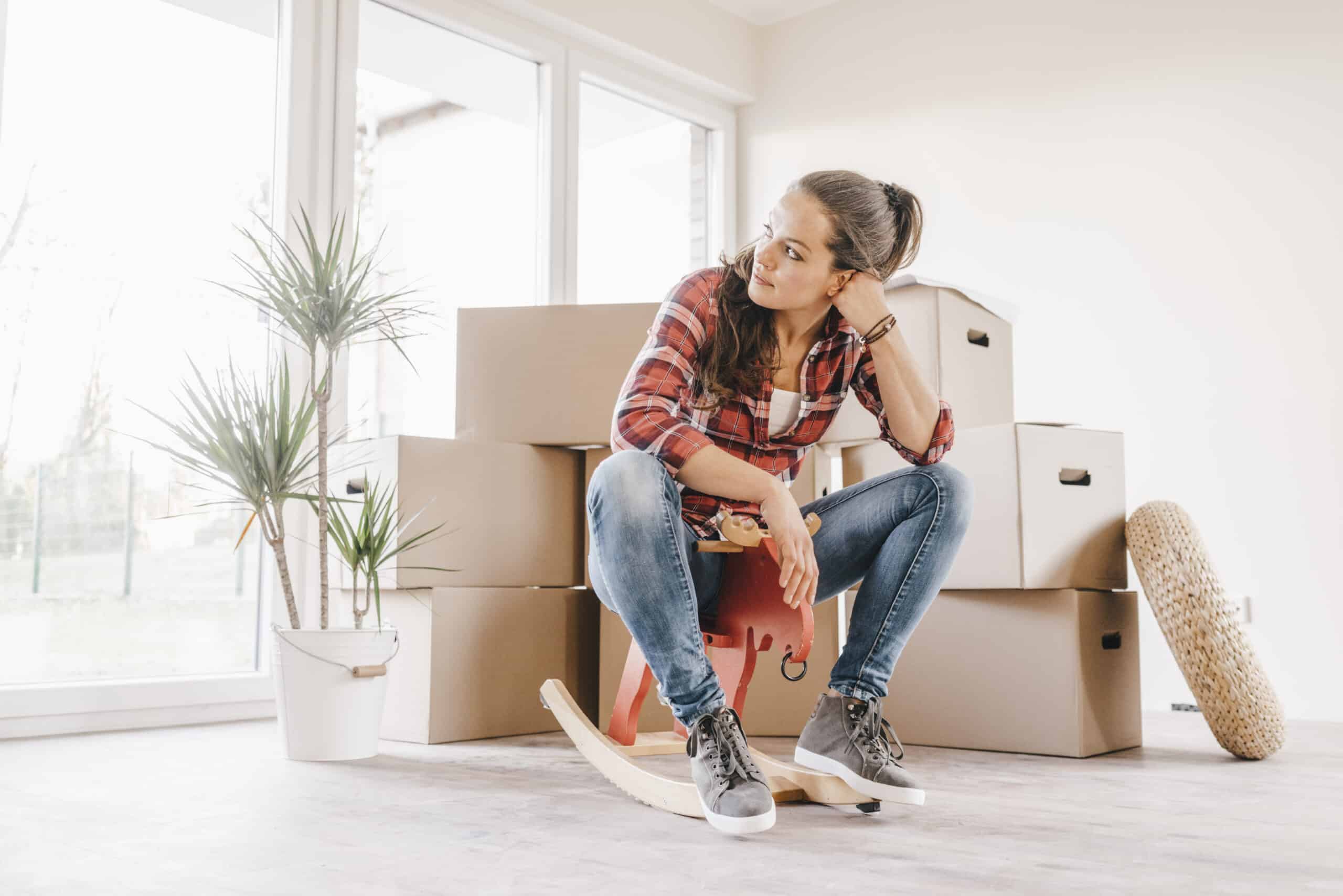 A woman sitting on a rocking chair in front of moving boxes, symbolizing the final steps in the home buying process.