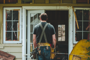 A man, equipped with a tool belt, stands in front of his house needing a home repair guide!