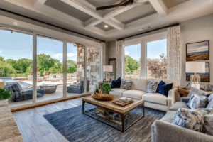 Bright living room with large windows, neutral furniture, a blue rug, and a view of a sunny patio area with outdoor seating and a pool.