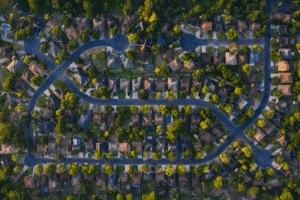 Aerial view of a suburban neighborhood showing curved streets, houses with driveways, and scattered green trees.