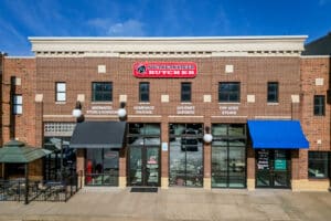 Brick storefront of Southern Steer Butcher with large red sign, multiple windows, awnings, and outdoor seating area on left side under blue sky.
