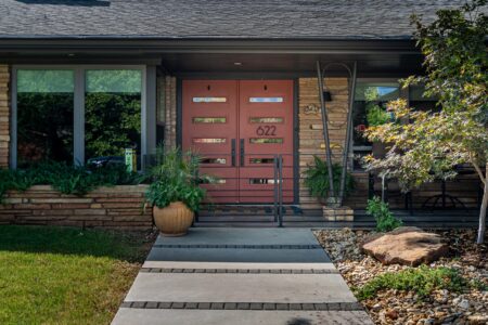 Contemporary house entry with red double doors, potted plants, pathway, stone landscaping, and house number 622 displayed next to a metal railing and tree—this rebuilt mid-century modern home at 622 Timber Lane Edmond OK exemplifies stylish living in the sought-after Clegern Edmond Oklahoma homes for sale.