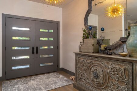 Modern entryway with double front doors, a rug, ornate wooden console table, decorative vases, and a large mirror reflecting a starburst light fixture—an inviting introduction to this beautifully rebuilt mid-century modern home.