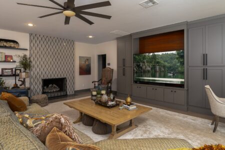 Modern living room with built-in gray cabinets, large TV, wooden coffee table, fireplace, and neutral-toned furnishings on a light carpeted floor—perfectly showcasing the stylish interiors often found in Clegern Edmond Oklahoma homes for sale.