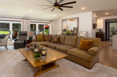A spacious living room with a large sectional sofa, coffee table, recliner, and wall art, featuring neutral tones and large windows overlooking a backyard—part of a beautifully rebuilt mid-century modern home at 622 Timber Lane Edmond OK.
