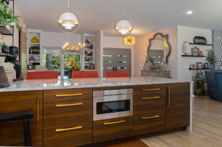 Modern kitchen with wood cabinets, gold handles, built-in microwave, marble countertop, and three orange barstools; open layout with visible dining and living areas—perfect for those searching for Clegern Edmond Oklahoma homes for sale.